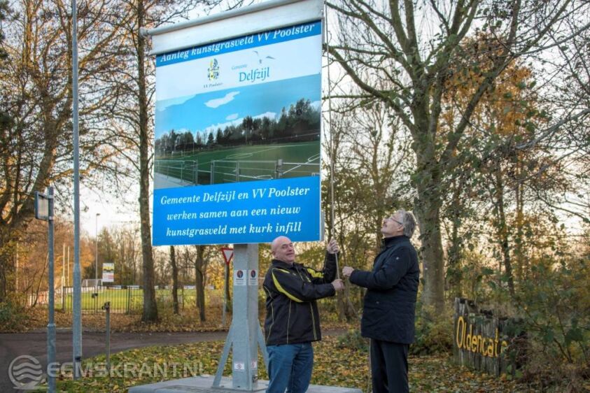 Wethouder Jan Menninga en Eltje Pijper onthullen met het bouwbord de start van de aanleg van het nieuwe kunstgrasveld