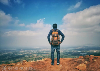 Foto door Sassu anas: https://www.pexels.com/nl-nl/foto/man-in-blauw-overhemd-en-blauwe-spijkerbroek-en-oranje-rugzak-staande-op-berg-klif-kijken-naar-stad-onder-blauwe-lucht-en-witte-wolken-732629/