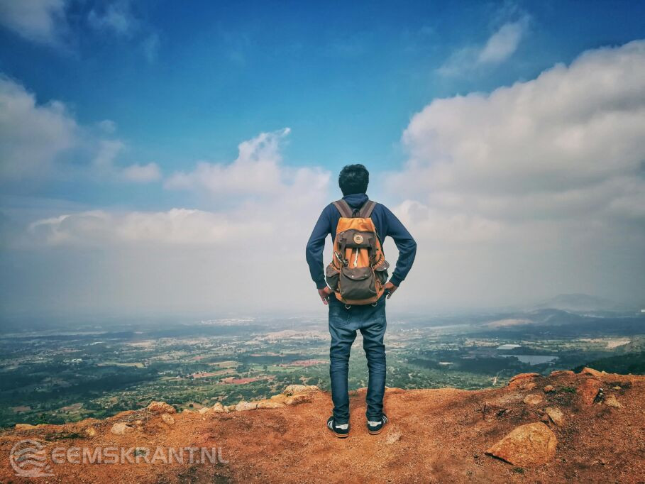 Foto door Sassu anas: https://www.pexels.com/nl-nl/foto/man-in-blauw-overhemd-en-blauwe-spijkerbroek-en-oranje-rugzak-staande-op-berg-klif-kijken-naar-stad-onder-blauwe-lucht-en-witte-wolken-732629/